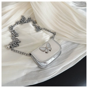 Detail of a mini silver metallic crossbody bag with a butterfly charm on satin fabric