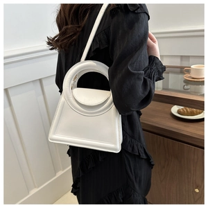Chic white trapezoid handbag with large round handle styled with a black dress in a cafe