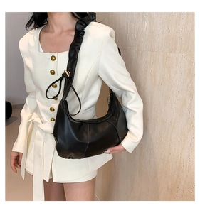 Détail du sac croissant noir avec bandoulière froncée sur une veste de blazer blanc