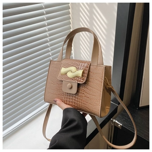Détail de la texture crocodile beige et du fermoir doré ondulé sur le sac