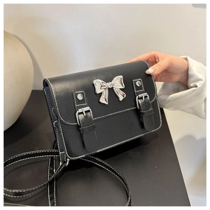 Détail d'un sac bandoulière noir avec boucle papillon argentée et coutures blanches