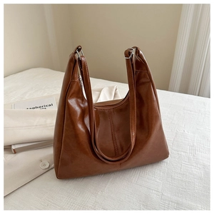 Close-up of brown PU leather tote bag with silver buckles on white textured surface