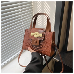 Détail d'un sac à main marron texture crocodile avec boucle métallique dorée ondulée