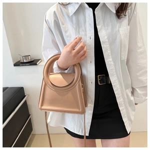 Chic khaki crossbody bag with unique circular handle shown on model in minimalist attire