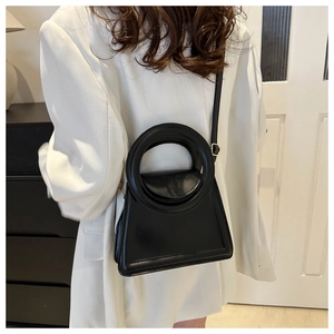 Fashionable black trapezoid crossbody bag with a unique large circular top handle