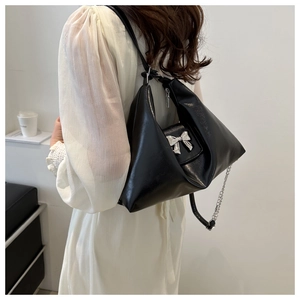 Detail of glossy black shoulder bag featuring a silver metal bow clasp and chain strap