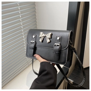 Détail du sac bandoulière en cuir noir avec boucle nœud argenté et coutures blanches