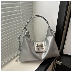 Detail of silver tote bag featuring a metallic bow ornament and zipper closure