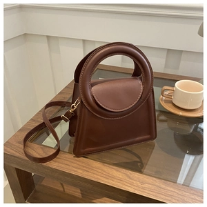 Detailed view of a brown faux leather crossbody bag with a round handle on a glass table