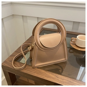 Detail view of khaki leather square bag with circular handle on a coffee table
