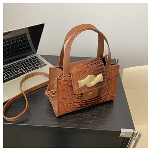 Détail de la texture cuir crocodile et du fermoir doré ondulé sur un sac à main marron