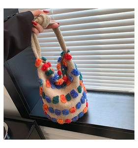 Close-up of knit bucket bag with colorful plush pom-poms on thick beige fabric