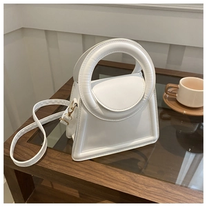 Detail of white minimalist handbag with large circular handle on a dark wooden table