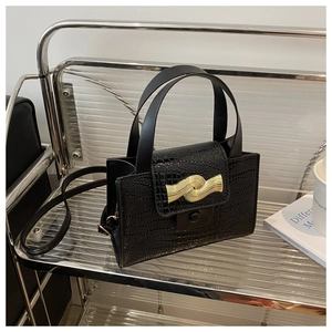 Détail d'un sac à main noir en similicuir avec texture crocodile et boucle dorée chic