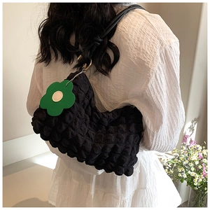 Detail of black popcorn texture shoulder bag featuring a green flower charm on a model