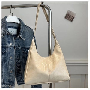 Close-up of cream Hobo bag on metal stand next to denim jacket with soft lighting