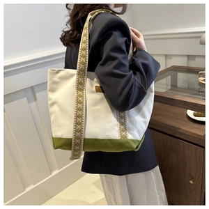 Détail d'un sac cabas en toile avec bandoulière tissée et base verte porté par un mannequin