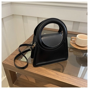 Detail of a black trapezoid leather handbag with round handle and gold hardware