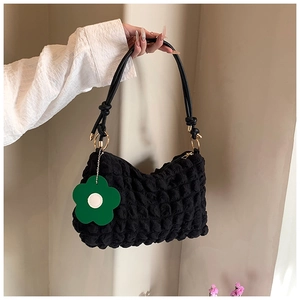 Detail of black popcorn texture shoulder bag with gold hardware and green floral charm