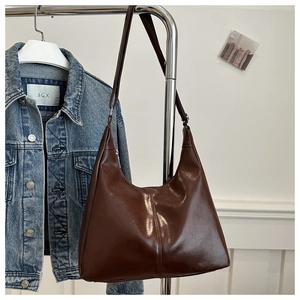 Detail of a dark brown glossy leather hobo bag hanging next to a denim jacket