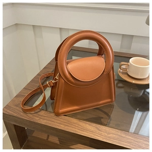Detail of caramel crossbody bag with round handle on a wooden table with a coffee cup
