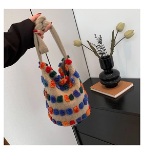 Detail view of plush bucket bag featuring colorful 3D pom-poms and knotted handle design