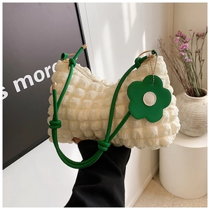 Close-up of textured bubble pleated shoulder bag with green woven strap and flower charm
