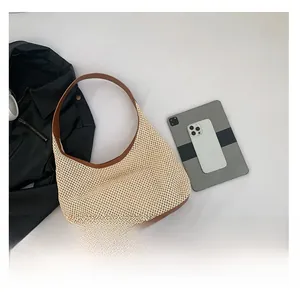 Flat lay of woven beige tote bag with brown leather strap and tech accessories