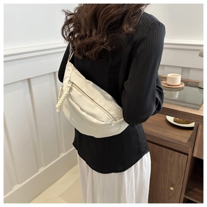 Detail of cream crescent waist bag featuring a stylish woven zipper pull decoration