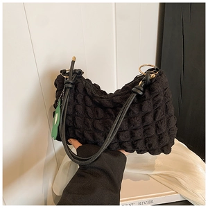 Detail of black bubble quilted texture on handbag with green leaf charm and gold ring