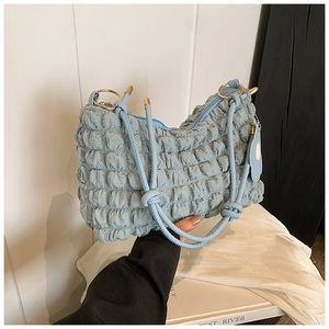 Detail of light blue pleated fabric shoulder bag with woven strap and gold metal rings
