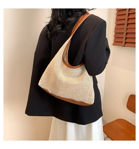 Detail of a beige hollow-out woven tote bag with brown leather handles worn by a model