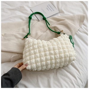 Detail of white popcorn texture bag with green rope handle and dinosaur pendant detail