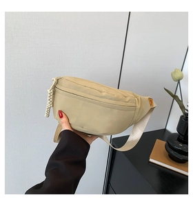 Detail of beige nylon crossbody bag featuring woven ball zipper and adjustable strap