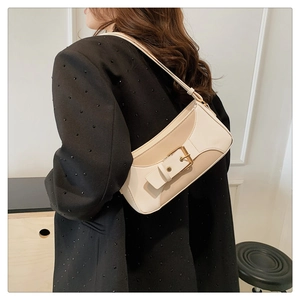 Side view of two-tone beige baguette bag with buckle detail on black blazer