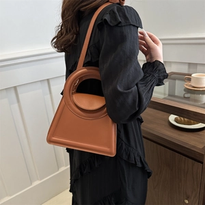 Minimalist caramel leather trapezoid handbag worn crossbody by a model in a stylish setting