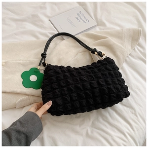 Close-up of black popcorn textured puff shoulder bag with a green floral charm detail