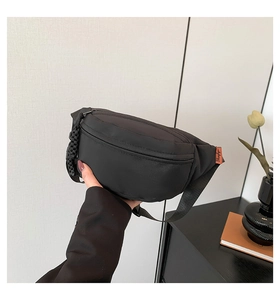 Detail of black nylon chest bag with orange letter label and adjustable strap