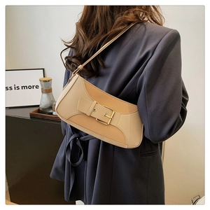Detailed view of light brown leather underarm bag with gold buckle worn by model