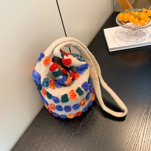 Beige knit bucket bag with colorful pom-poms and shoulder strap on a wooden table