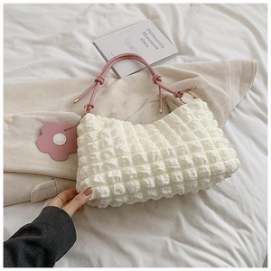 Detail of white quilted bubble texture handbag with pink rope handles and flower charm