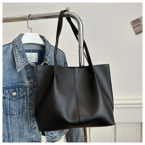 Detail of a black leather tote bag with vertical stitching hanging on a metal rack