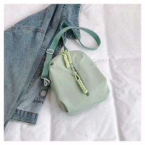 Close-up of mint green nylon crossbody bag with woven rope zippers and adjustable strap