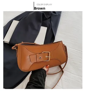 Detail view of brown leather baguette bag featuring a large gold buckle and slim strap