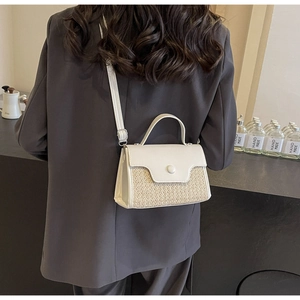 Detail of a woven textured small crossbody bag featuring a smooth white flap and top handle