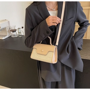 Detail of woven straw and beige leather shoulder bag worn over a grey blazer jacket