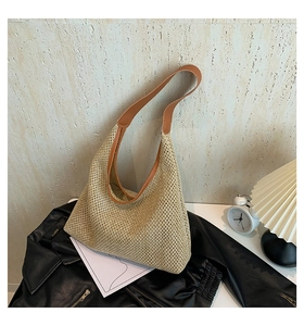 Close-up of woven straw tote bag with brown faux leather handles on a black jacket