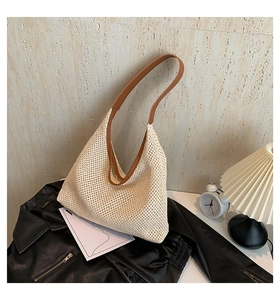 Close-up of beige woven tote bag with brown leather straps against a stone wall