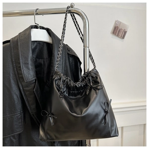 Détail d'un sac plissé noir avec cordon, nœuds décoratifs et bandoulière en chaîne métal