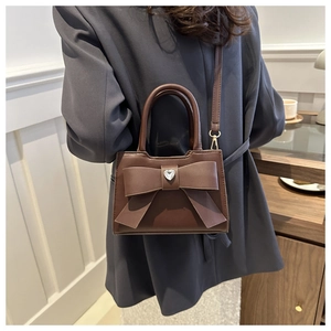 Dettaglio di una piccola borsa quadrata marrone con fiocco e strass a cuore su modella